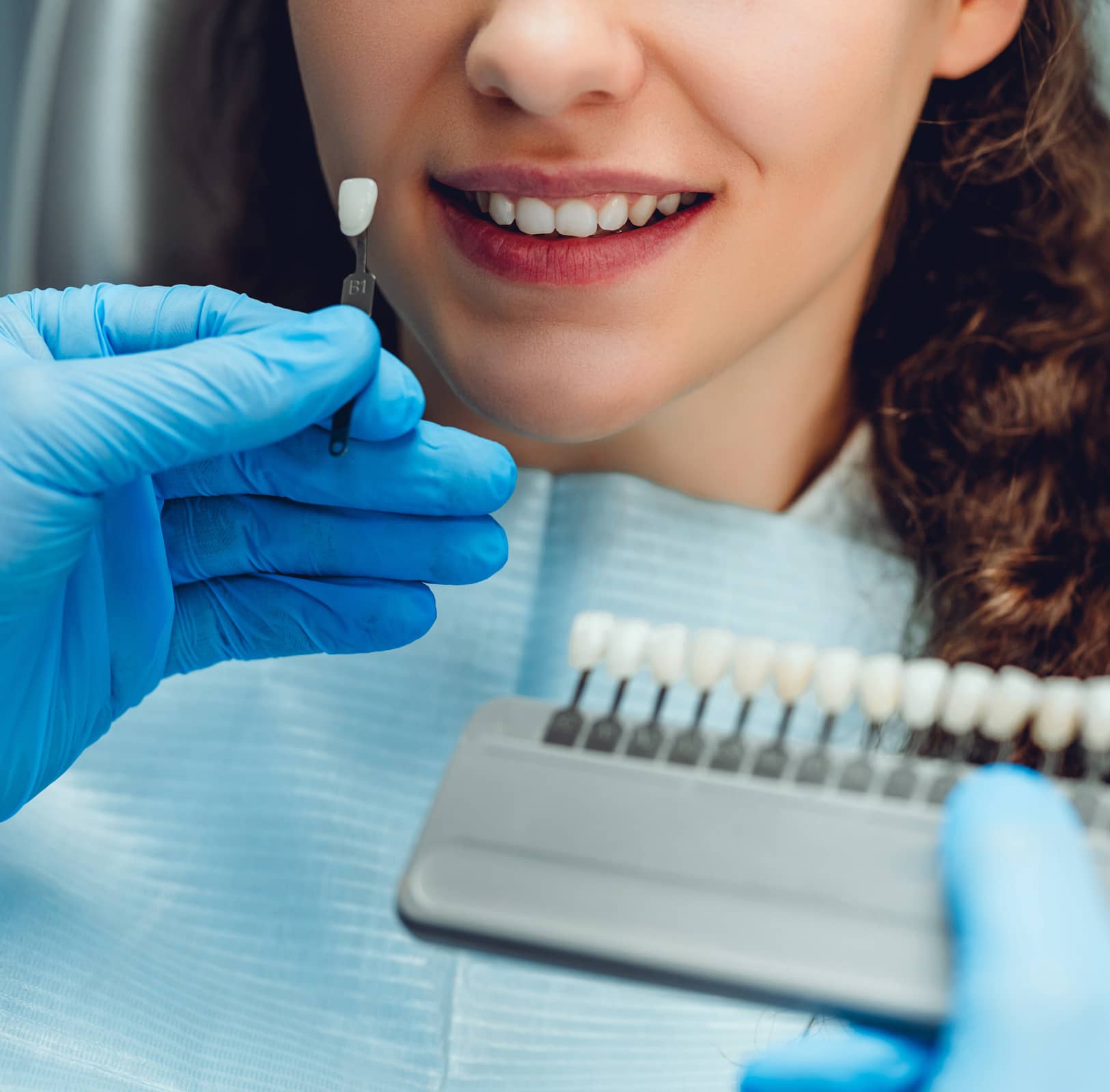 Dentist checking and selecting color of young womans teeth